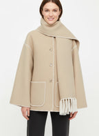 Frau trägt einen beigen Mantel mit integriertem Schal und kontrastierenden Nähten vor weißem Hintergrund