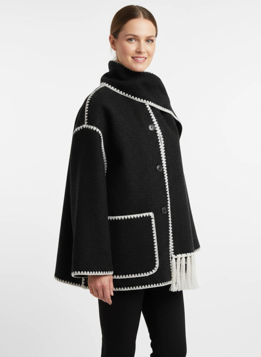 Frau trägt einen schwarzen Poncho-Schalmantel mit weißen Fransen und kontrastierenden Nähten vor weißem Hintergrund