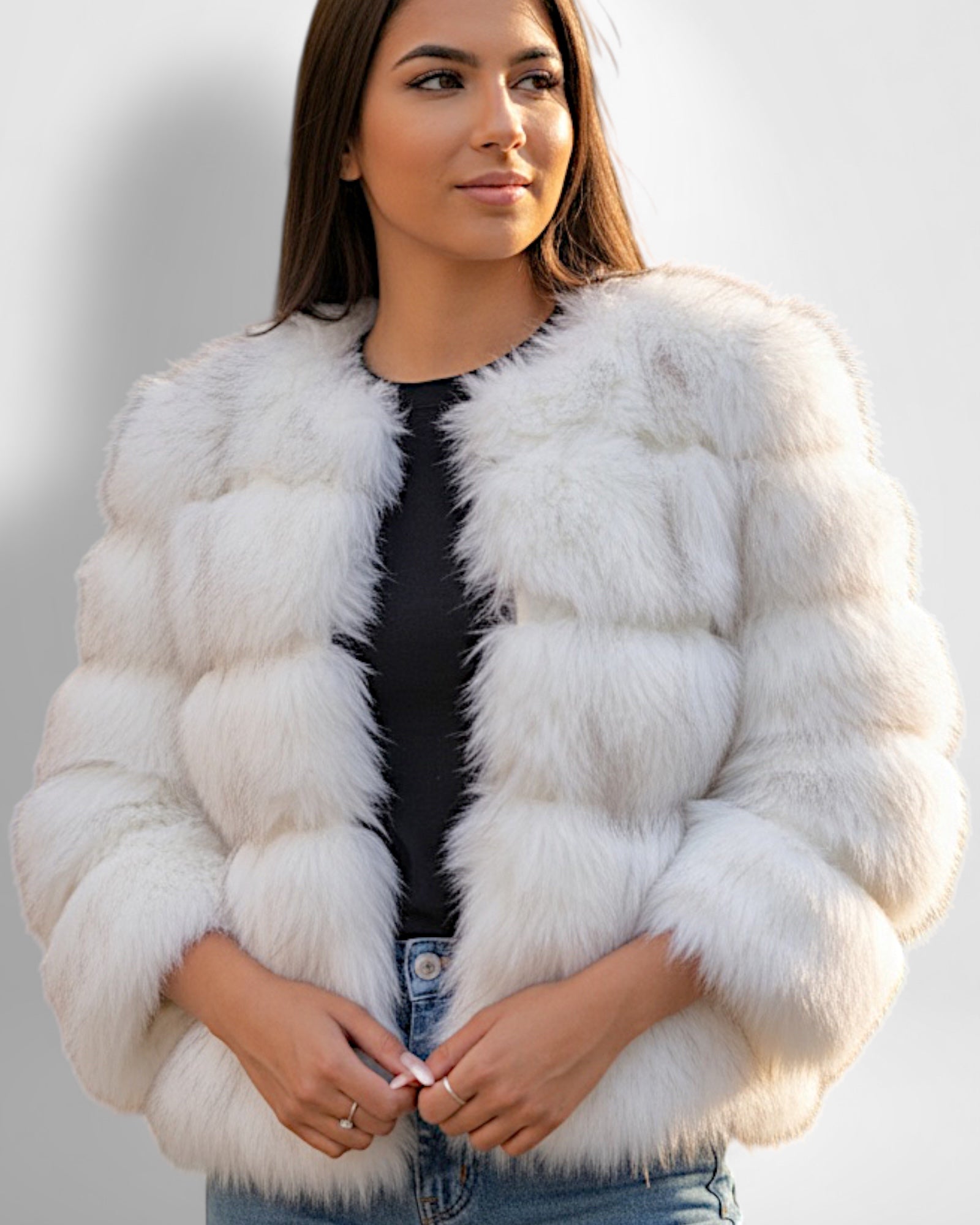 Frau trägt eine weiße Webpelzjacke vor einfarbigem Hintergrund
