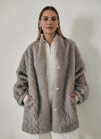 Frau trägt eine graue Plüschjacke über einem weißen Pullover vor einfarbigem Hintergrund