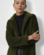 Frau trägt einen grünen Mantel vor weißem Hintergrund