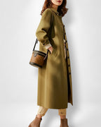 Frau trägt einen langen olivgrünen Mantel mit vielen schwarzen Knöpfen und hält eine braune Handtasche vor weißem Hintergrund