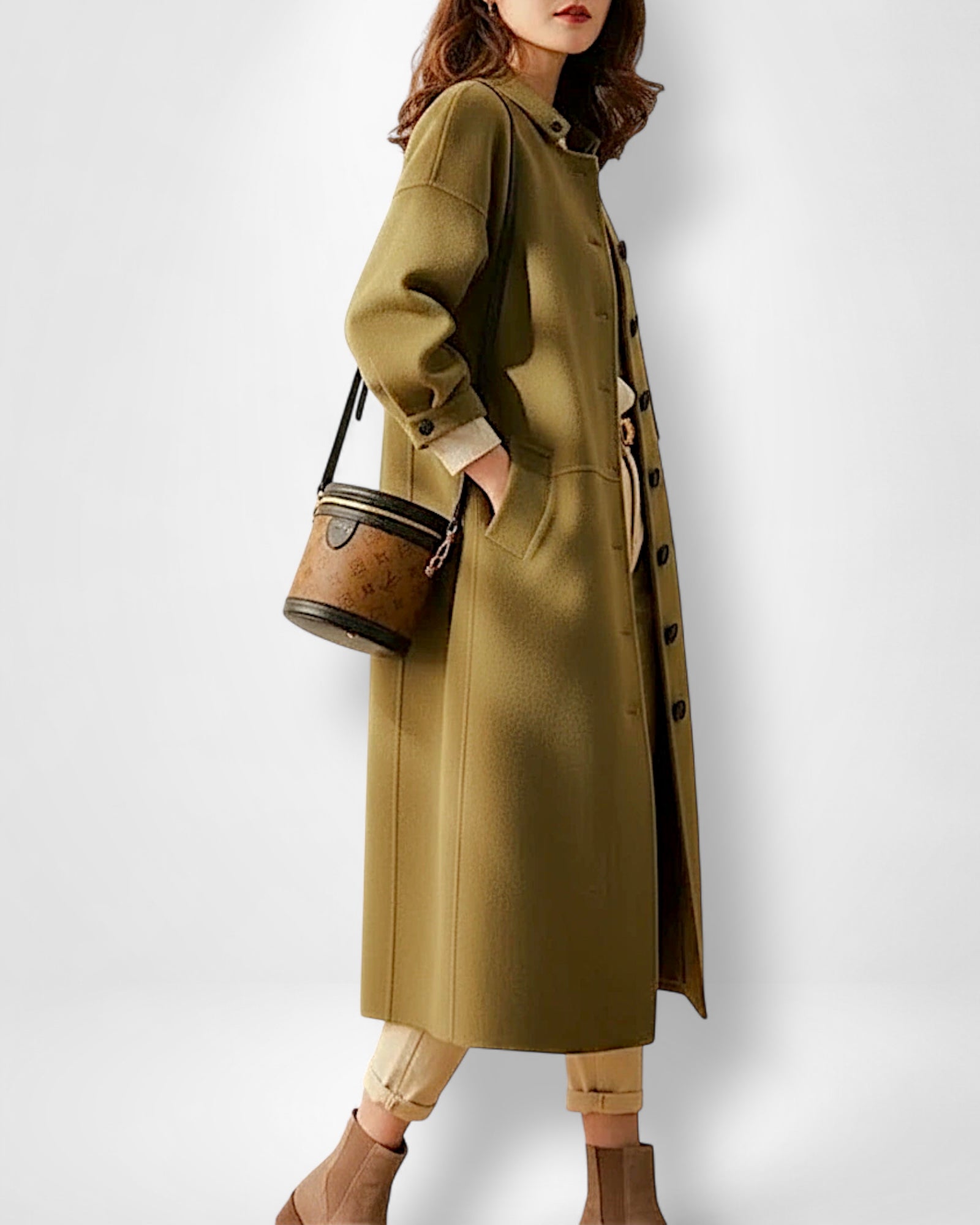 Frau trägt einen langen olivgrünen Mantel mit vielen schwarzen Knöpfen und hält eine braune Handtasche vor weißem Hintergrund