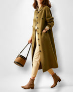 Frau trägt einen langen olivgrünen Mantel mit eleganter Brusttasche vor weißem Hintergrund