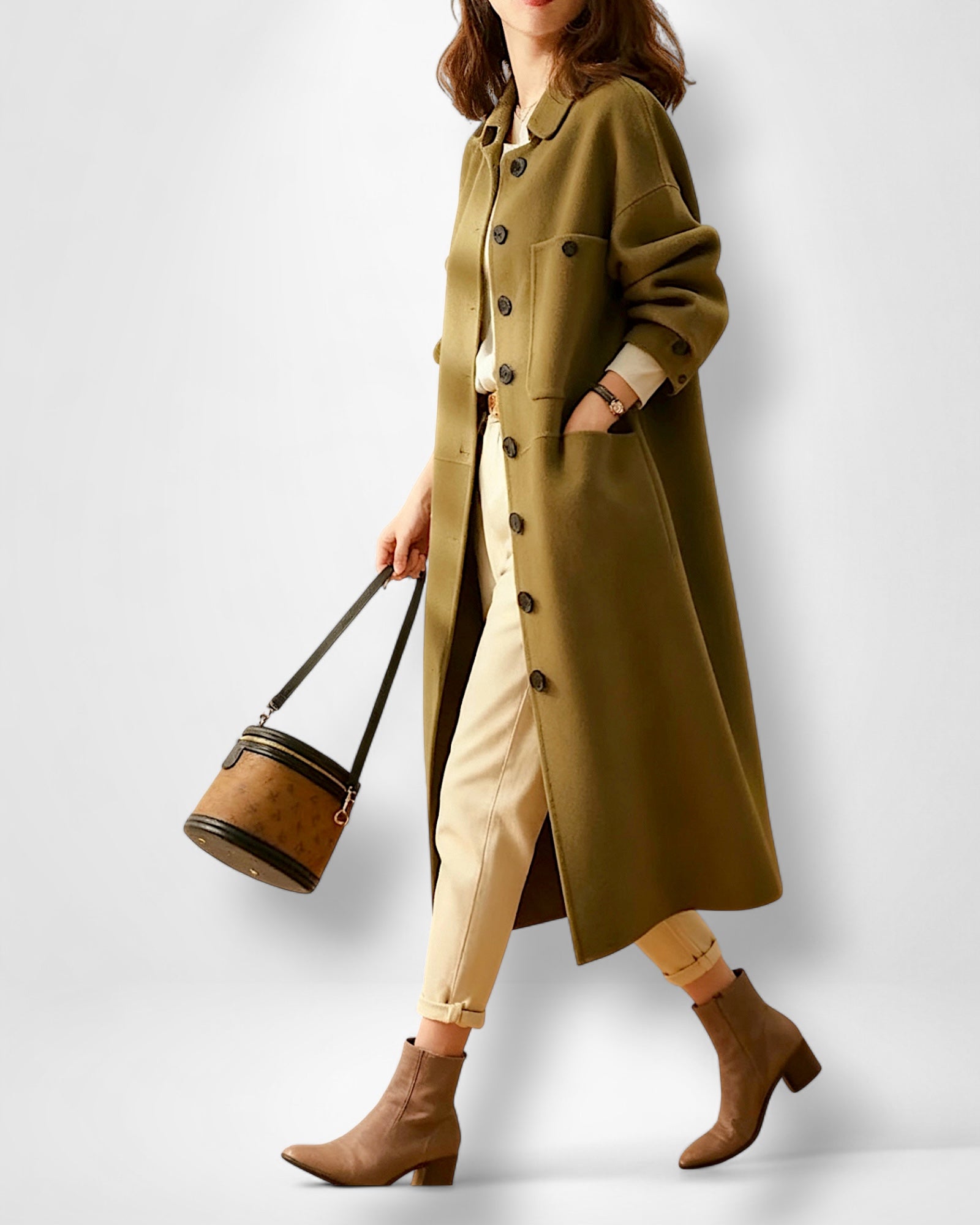 Frau trägt einen langen olivgrünen Mantel mit eleganter Brusttasche vor weißem Hintergrund