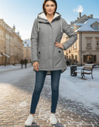 Frau in voller Länge mit grauer Winterjacke mit Kapuze und weichem Futter an einem sonnigen Wintertag in der Stadt