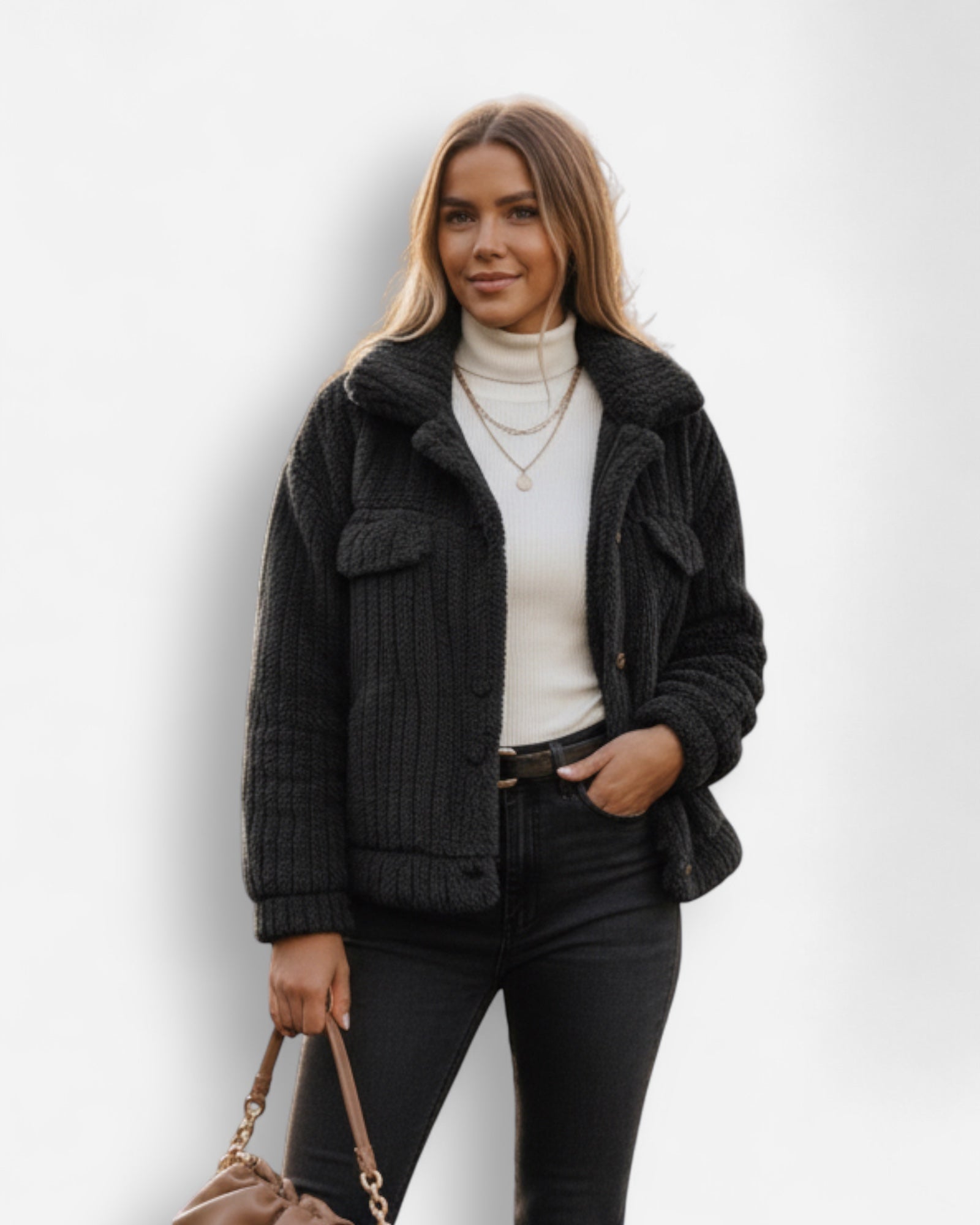 Frau trägt eine kurze schwarze Teddyjacke über einem weißen Rollkragenpullover und einer schwarzen Hose