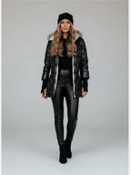 Frau trägt eine schwarze Pufferjacke, eine schwarze Hose und eine schwarze Mütze vor weißem Hintergrund