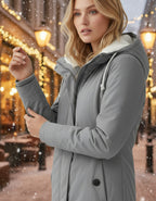 Frau trägt eine warme Winterjacke mit Kapuze und weichem Futter in Grau in winterlicher Stadtumgebung bei gemütlicher Atmosphäre