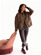 Frau trägt eine Übergangsjacke mit Leopardenmuster, vor einem rosa Hocker auf weißem Hintergrund