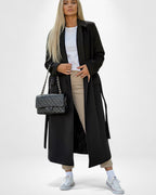 Frau trägt einen schwarzen klassischen Mantel vor weißem Hintergrund