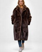 Frau trägt einen braunen Maxi-Webpelzmantel vor weißem Hintergrund 0