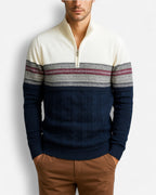 Mann trägt einen dunkelblauen und cremefarbenen Half-Zip-Pullover mit Zopfmuster und nordischem Design vor hellgrauem Hintergrund