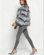 Frau in grauer flauschiger Kurzjacke und grauem Outfit vor weißem Hintergrund