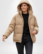 Frau trägt eine beige Pufferjacke mit Kapuze vor weißem Hintergrund