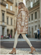 Frau geht eine Stadtstraße entlang und trägt eine beige glänzende Pufferjacke mit Kapuze