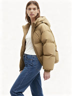 Frau trägt eine beige Steppjacke und blaue Jeans vor weißem Hintergrund