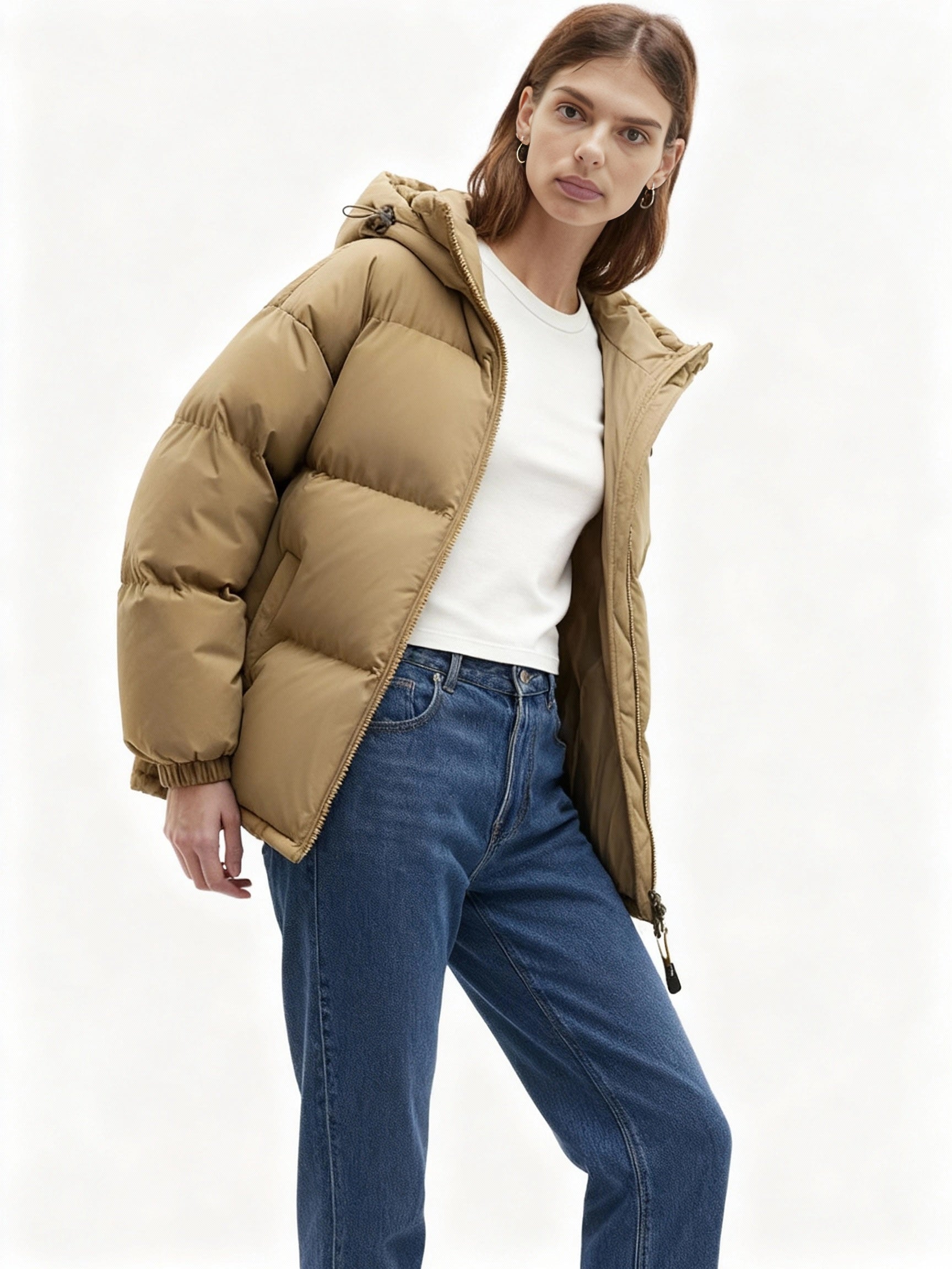 Frau trägt eine Winterjacke mit Kapuze und blauer Jeans vor weißem Hintergrund