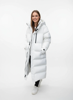 Frau im sportlich-legeren Stil trägt einen langen weißen Puffermantel vor weißem Hintergrund