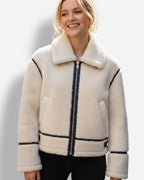 Frau trägt eine weiße Sherpa-Jacke mit schwarzen Akzenten vor weißem Hintergrund