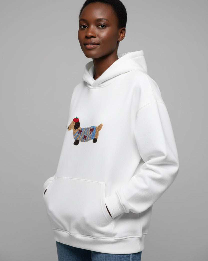 Junge Frau trägt einen weißen Hoodie mit Dackelmotiv vor schlichtem Hintergrund