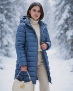 Frau trägt eine blaue Pufferjacke in einem verschneiten Wald