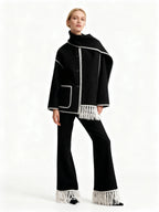 Frau trägt einen schwarzen Schal-Mantel mit weißen Fransen-Details vor weißem Hintergrund