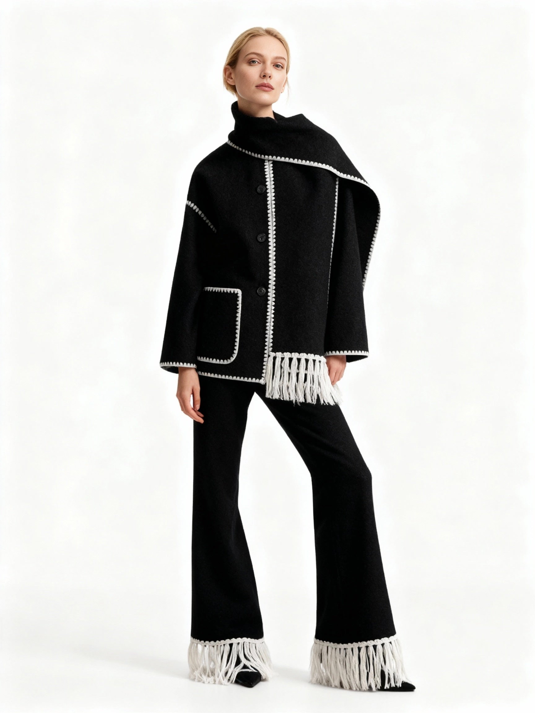 Frau trägt einen schwarzen Schal-Mantel mit weißen Fransen-Details vor weißem Hintergrund