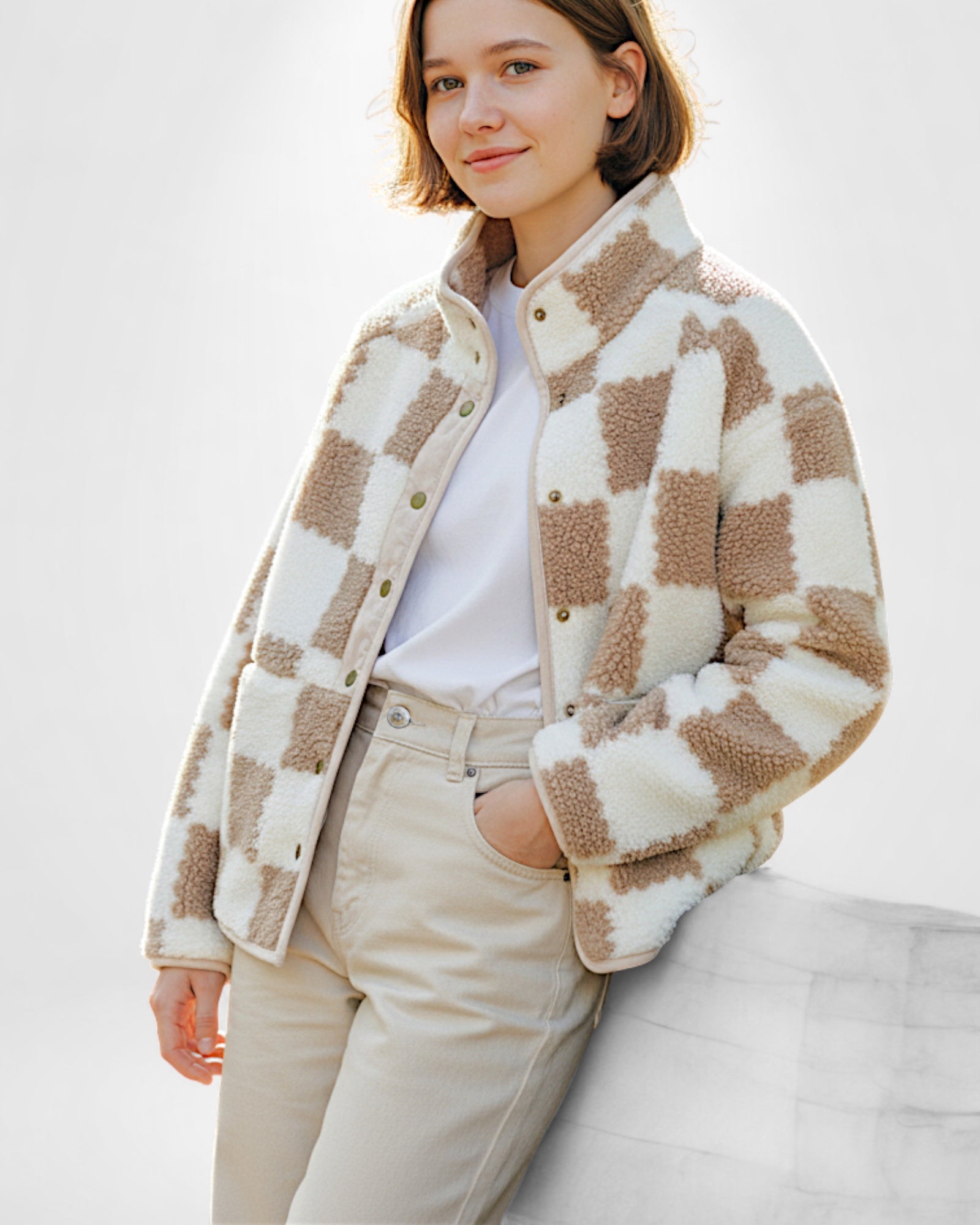 Frau trägt eine beige-weiß karierte Sherpa-Fleecejacke mit Reißverschlusstaschen vor einfarbigem Hintergrund