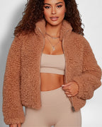 Frau trägt eine braune Sherpa-Jacke vor einfarbigem Hintergrund