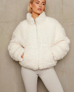 Person trägt eine weiße flauschige Jacke vor neutralem Hintergrund