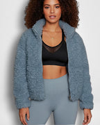 Frau trägt eine blaue Sherpa-Jacke und passende Leggings vor weißem Hintergrund