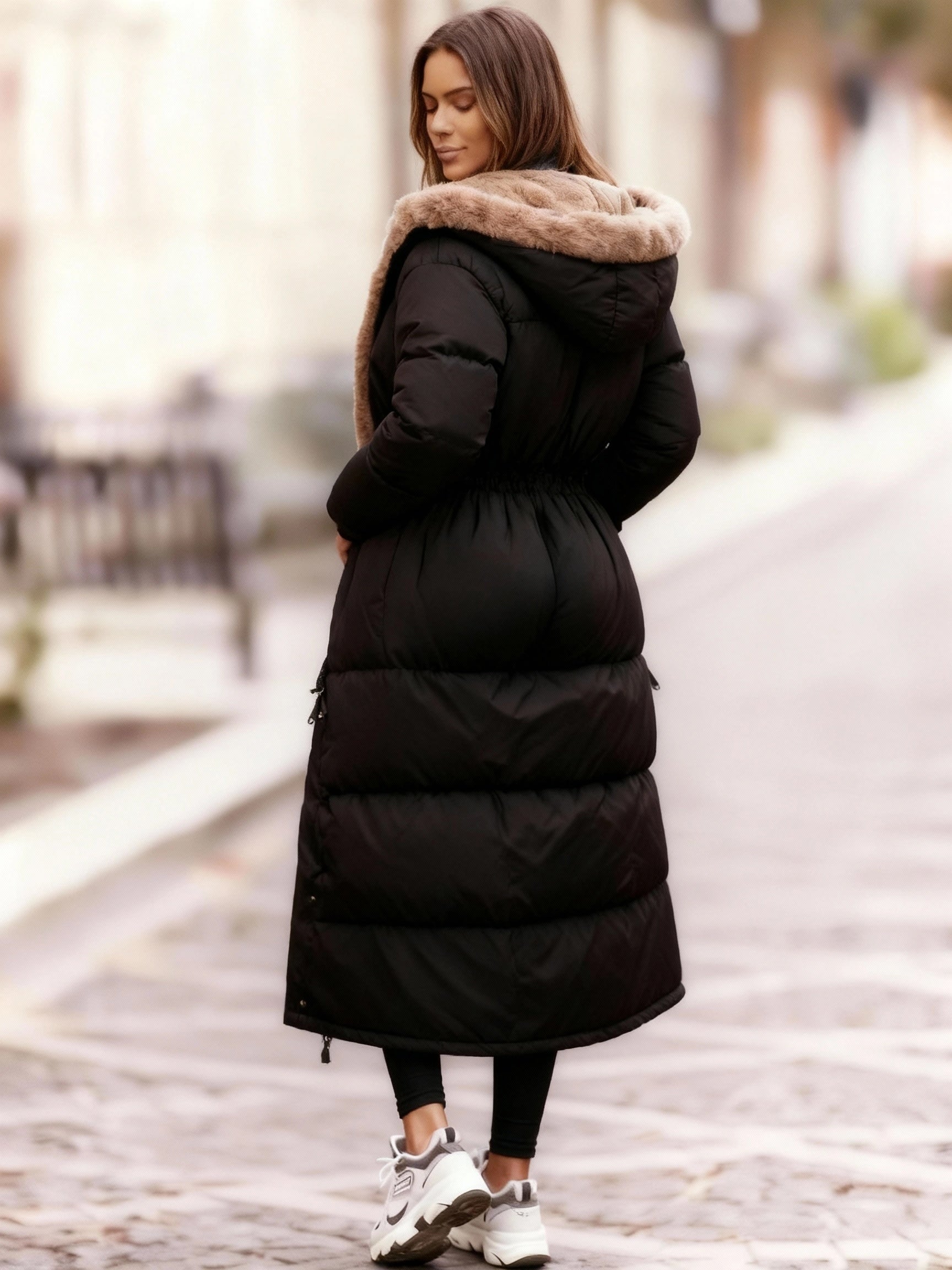 Frau trägt einen langen schwarzen Steppmantel vor unscharfem Straßenhintergrund