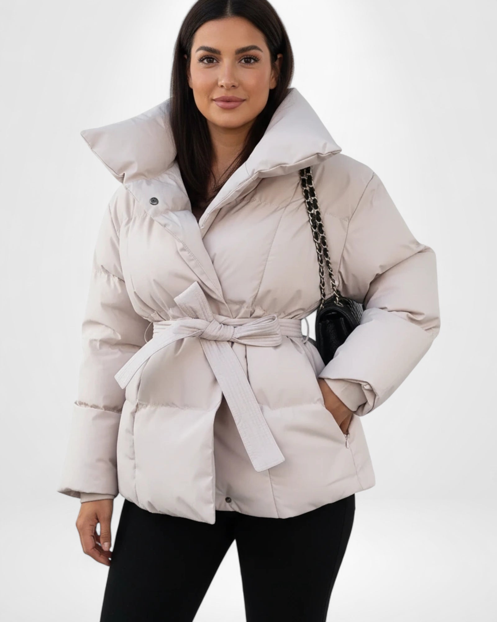 Frau trägt eine beige Pufferjacke mit Gürtel vor weißem Hintergrund