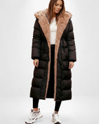 Frau trägt einen langen schwarzen Steppmantel mit braunem Kunstpelzbesatz vor weißem Hintergrund