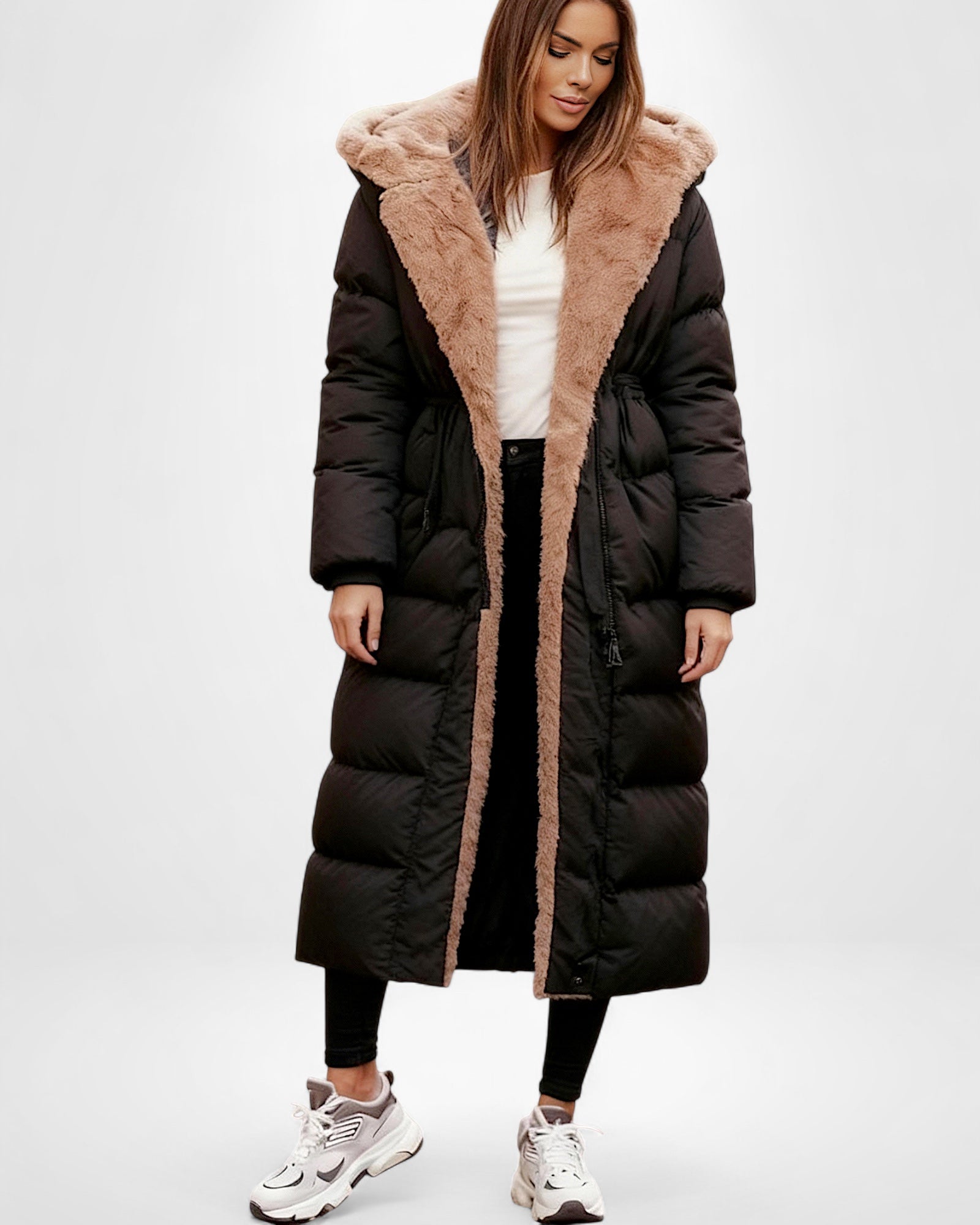 Frau trägt einen langen schwarzen Steppmantel mit braunem Kunstpelzbesatz vor weißem Hintergrund