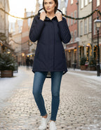 Frau in voller Länge mit marineblauer Winterjacke mit Kapuze und weichem Futter an einem sonnigen Wintertag in der Stadt