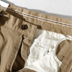 Nahaufnahme einer beigen Hose mit Knopf und Lasche auf weißem Hintergrund.