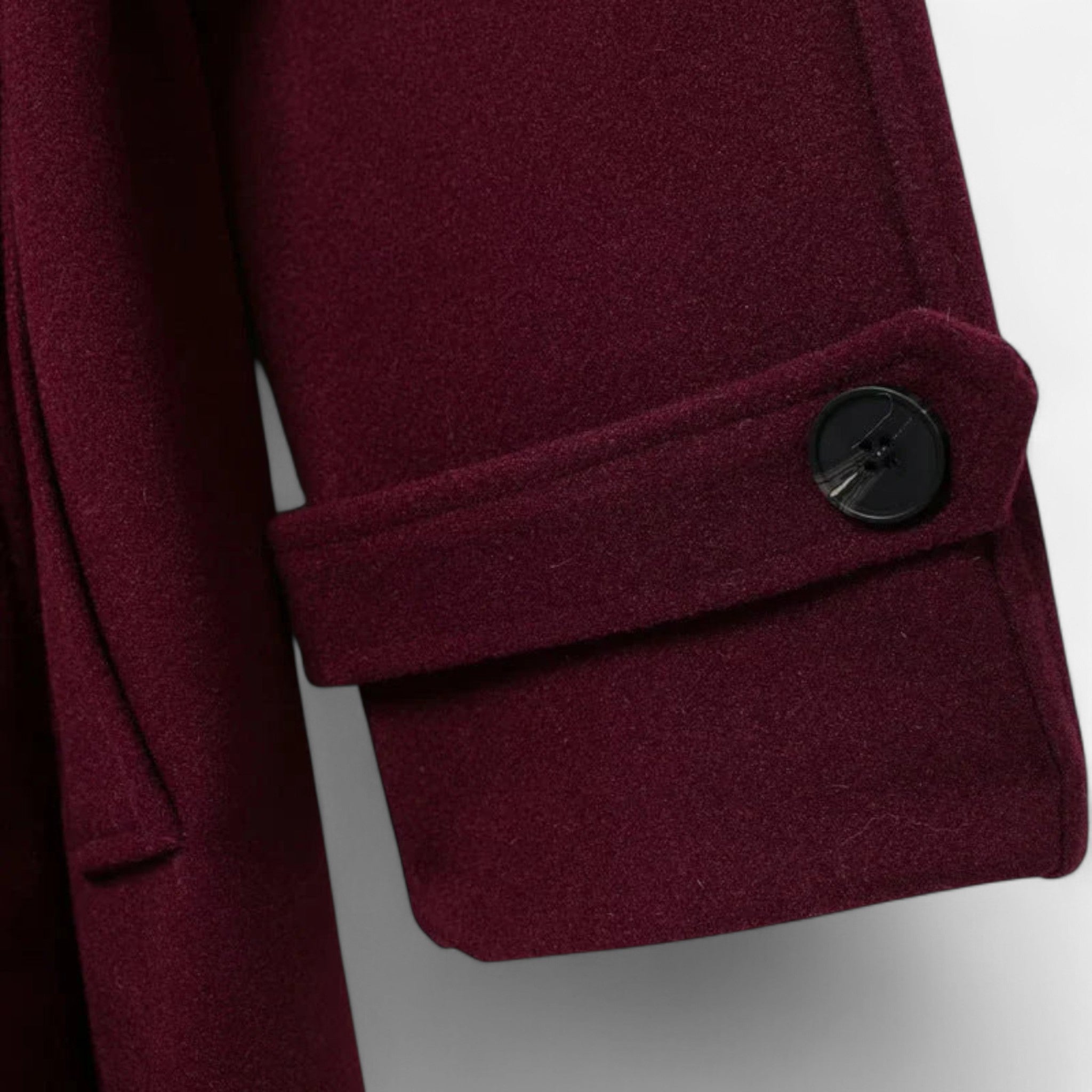 Nahaufnahme eines burgunderfarbenen Mantels mit Knopf vor hellgrauem Hintergrund