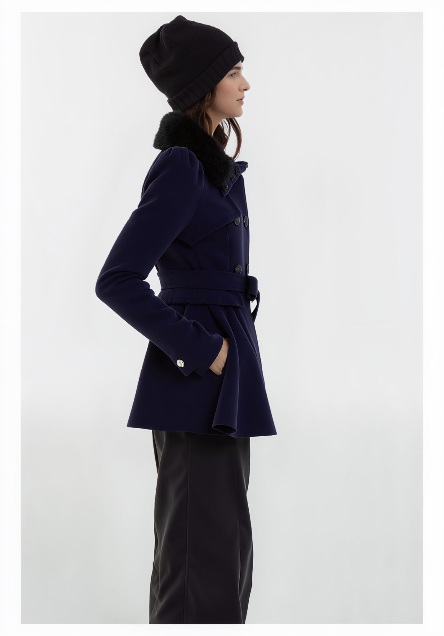 Person trägt einen marineblauen Mantel und eine schwarze Mütze vor weißem Hintergrund