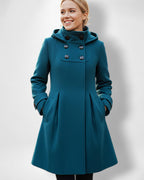 Frau trägt einen taillierten petrolblauen Mantel mit Stehkragen vor hellgrauem Hintergrund