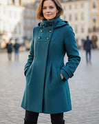 Frau trägt einen mittellangen petrolblauen Doppelknopf-Mantel und steht auf einer Stadtstraße