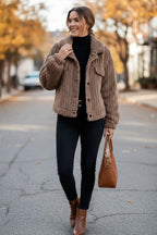 Frau trägt eine kurze braune Sherpa-Strickjacke, einen schwarzen Rollkragenpullover, dunkle Jeans und braune Stiefel und hält eine braune Handtasche auf einer Straße
