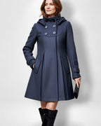 Frau trägt einen schwarzen A-Linien-Mantel vor weißem Hintergrund