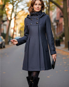 Frau trägt einen schwarzen eleganten Mantel mit Kapuze und Stehkragen auf einer Straße mit unscharfem Hintergrund