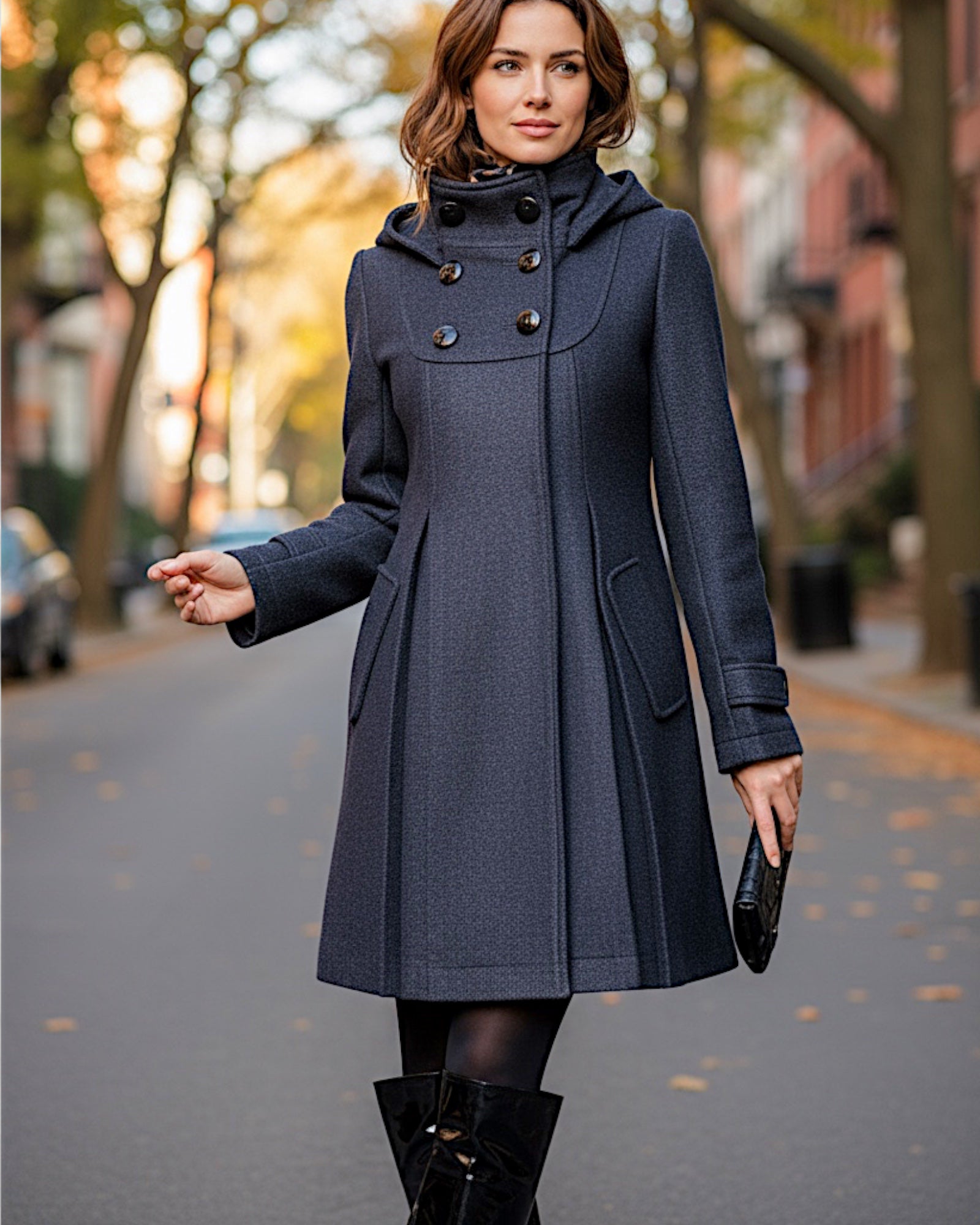 Frau trägt einen schwarzen eleganten Mantel mit Kapuze und Stehkragen auf einer Straße mit unscharfem Hintergrund