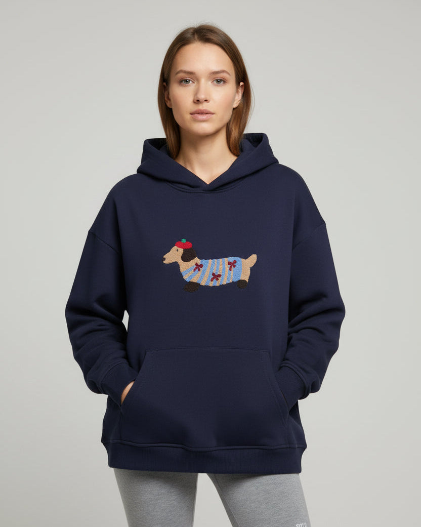 Junge Frau trägt einen marineblauen Hoodie mit Dackelmotiv vor schlichtem Hintergrund