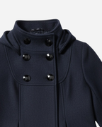 Nahaufnahme eines schwarzen Mantels mit schwarzen Knöpfen vor hellgrauem Hintergrund