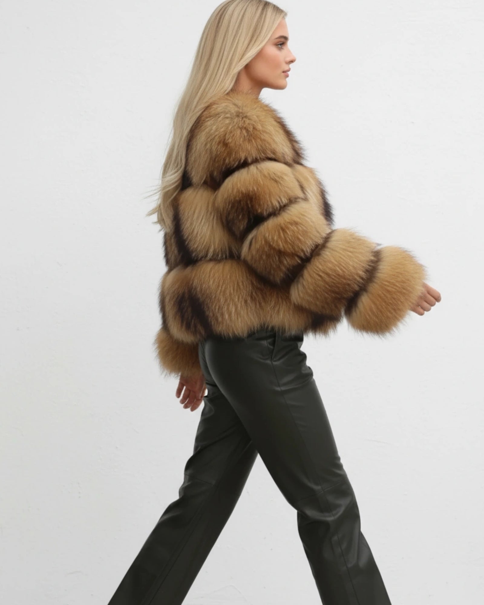 Frau in braunem flauschigem Kurzmantel und schwarzer Lederhose vor weißem Hintergrund