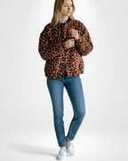 Frau trägt eine kurze Jacke mit Leopardenmuster und eine blaue Jeans vor weißem Hintergrund